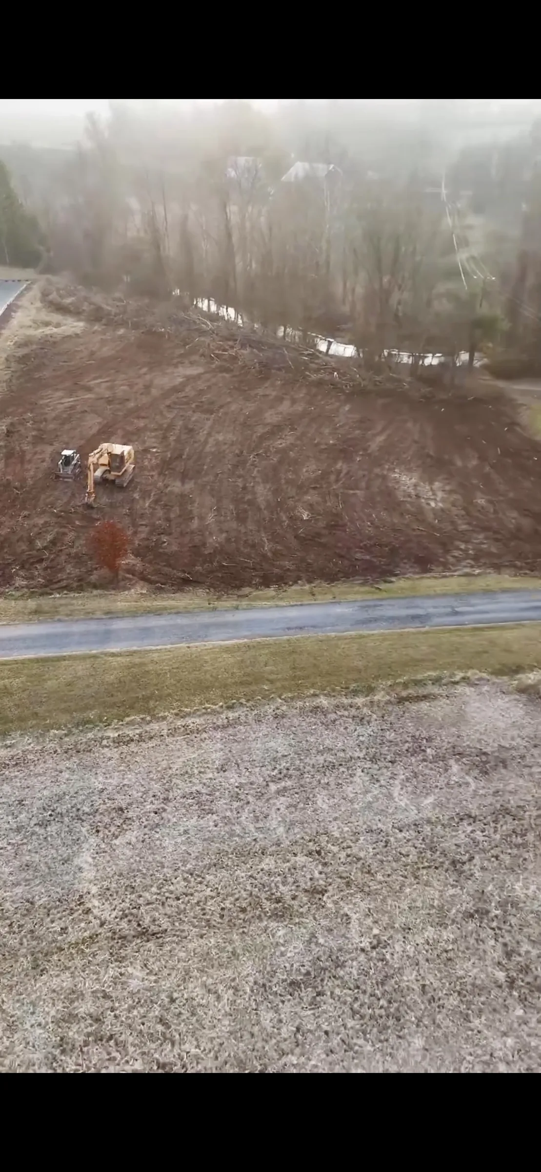 Freshly cleared rural lot with surface drainage and a misty wooded backdrop