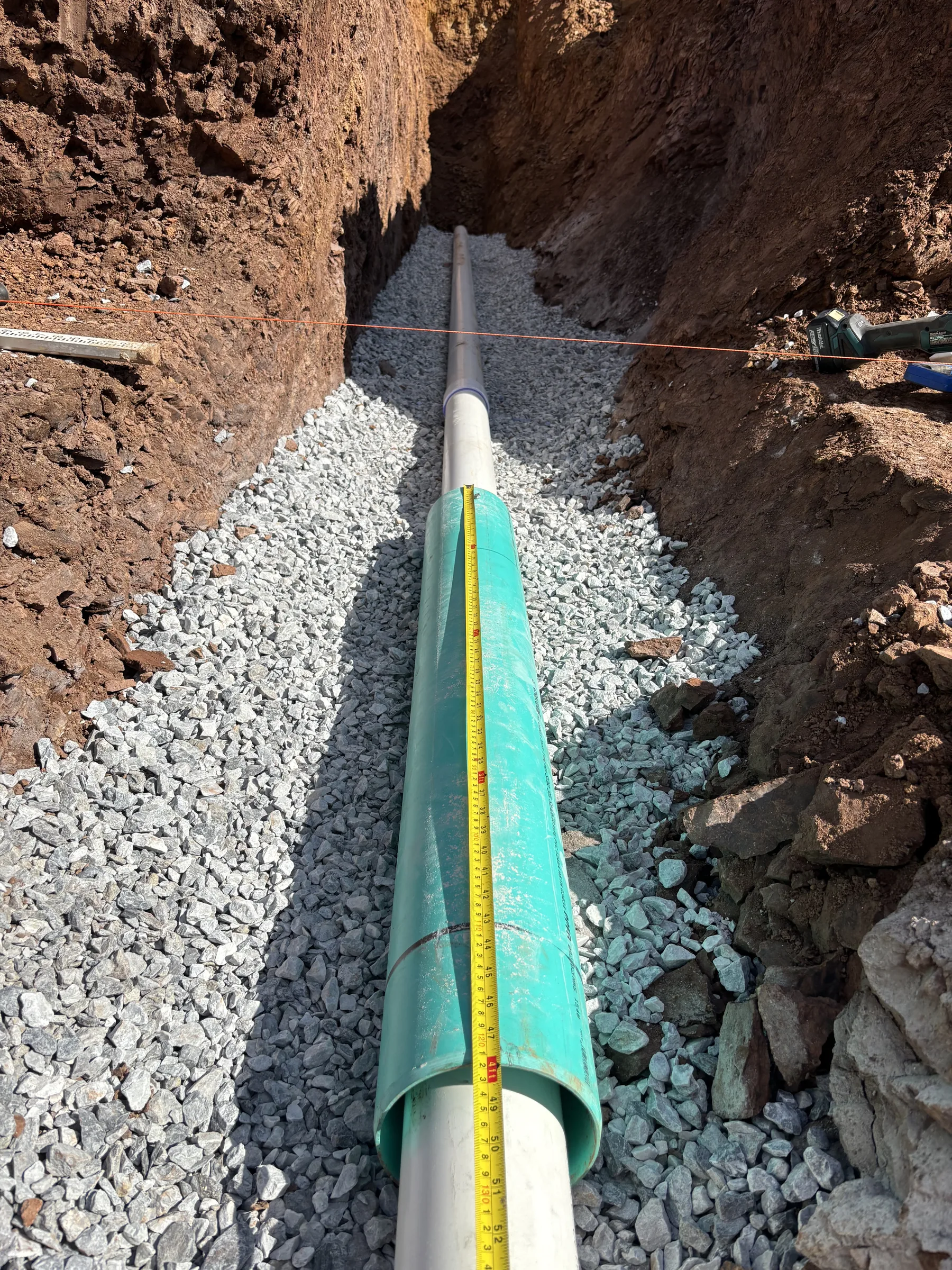 Green PVC utility pipe seated in a gravel-bedded trench