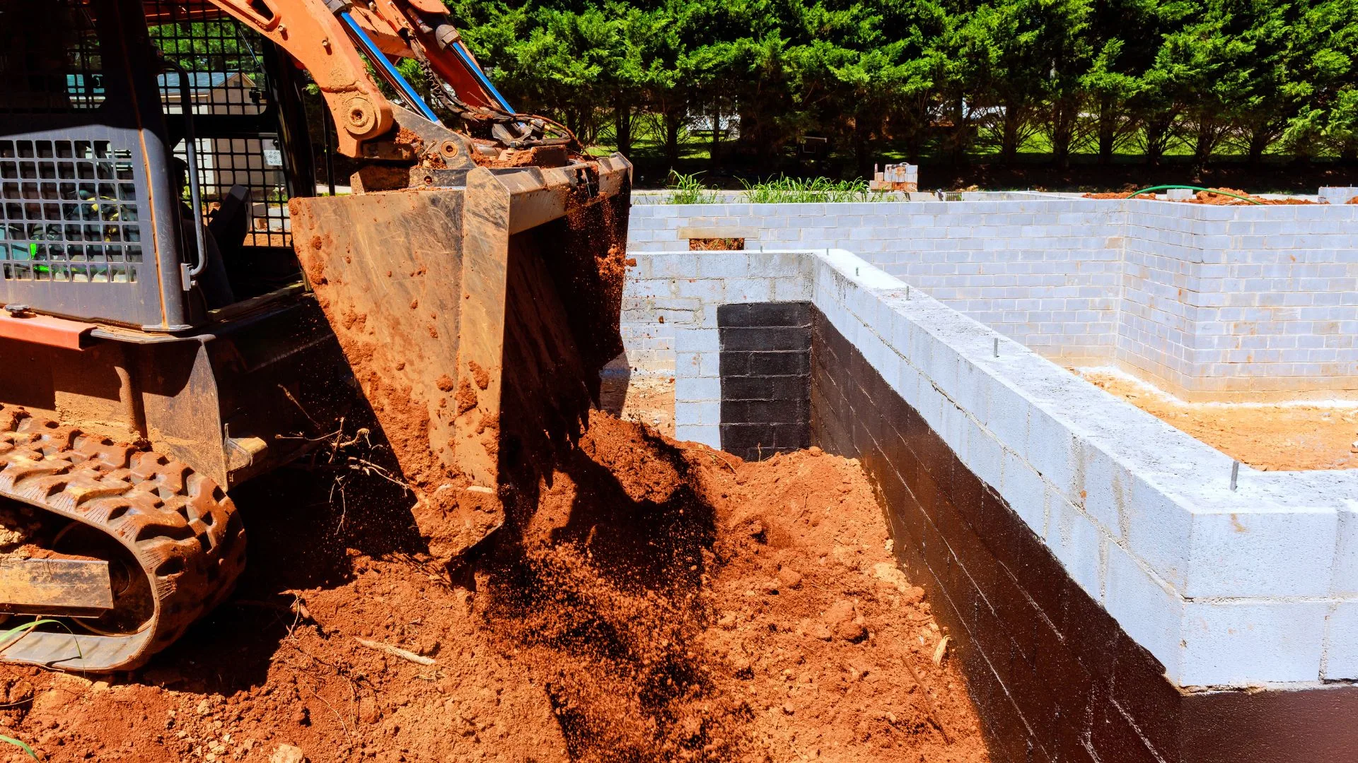 Skid steer placing fill at a foundation excavation site